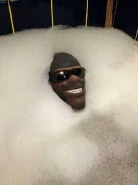 A disembodied mannequin head wearing sunglasses smiling from the middle of a bubble bath.