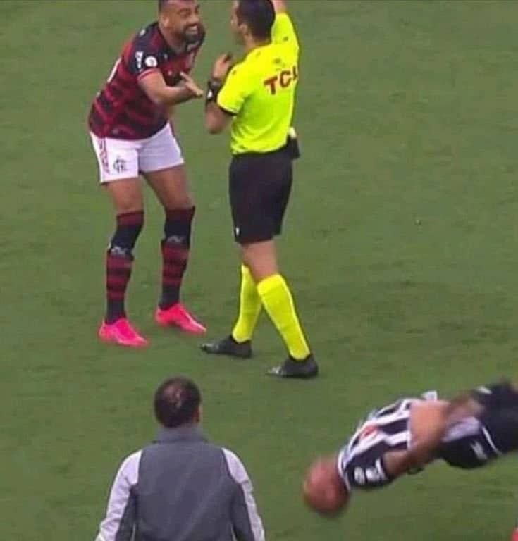 A soccer player executing a dynamic backflip on the pitch while a referee watches closely.