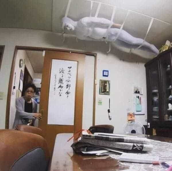 A person in a full white morph suit taped securely to a dining room ceiling.