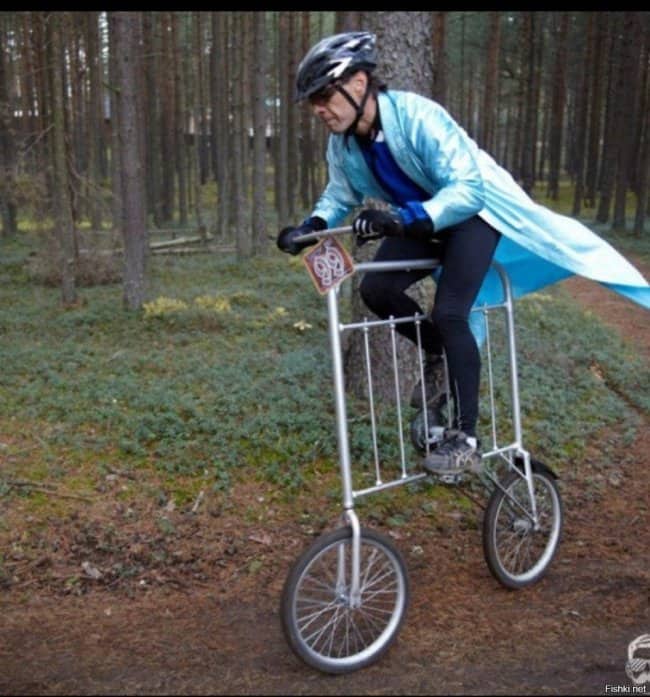 A cyclist in a blue coat riding a custom tall bicycle built from a metal bed frame.