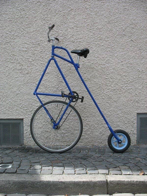 A custom blue bicycle with a massive front wheel and a tiny trailing rear wheel.