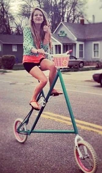 A young woman riding a highly unorthodox tall bicycle with an oversized triangular green frame.