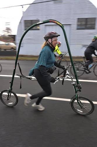 A woman running while suspended inside a bizarre, giant arched bicycle frame without any pedals.