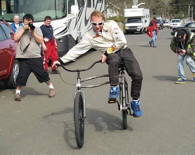 A man in racing gear posing on a custom wide-set bicycle with a split side-by-side wheel design.