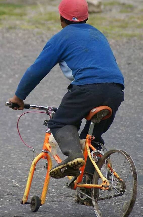 A child riding an orange bicycle that has an absurdly tiny wheel on the front fork.
