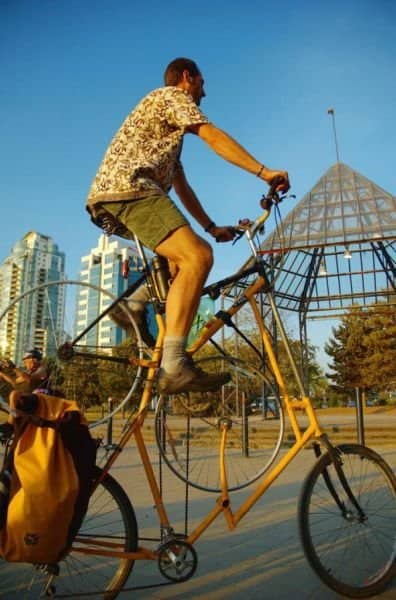A cyclist riding a monstrous double-stacked tall bike with additional bicycle frames welded inside.