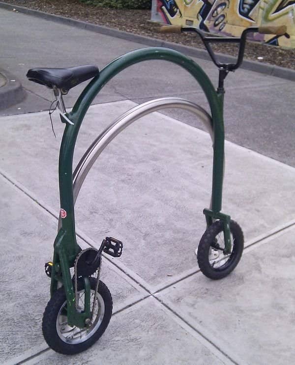 A stationary custom bicycle with a continuous circular green metal frame and tiny wheels.