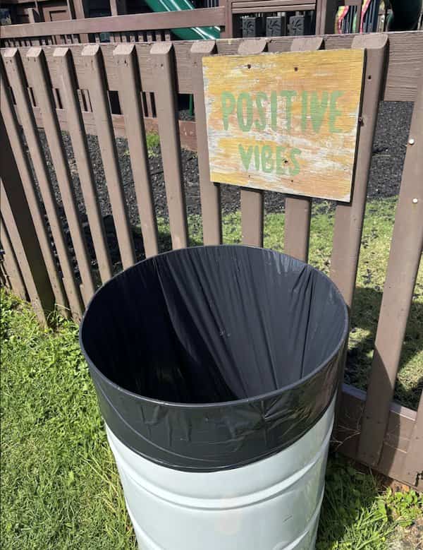Trash can with black liner placed directly below a faded sign reading positive vibes.
