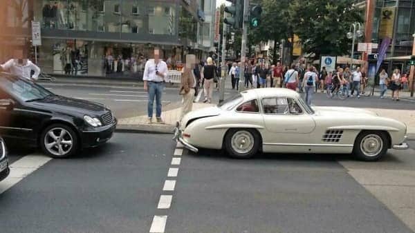 A classic white Mercedes-Benz 300SL Gullwing involved in a minor traffic accident on a city street.