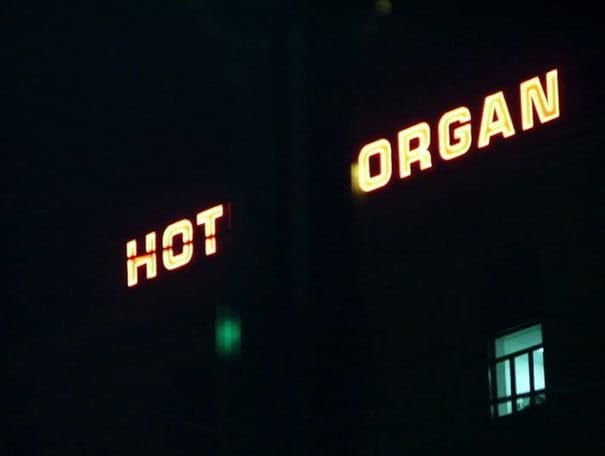 Glitching hot organ neon sign glowing red and yellow in the dark night.