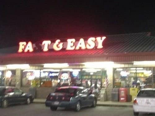 A broken Fast and Easy neon sign reading FAT & EASY at night.