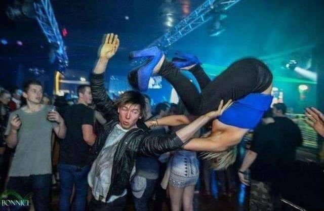 Man drop-lifting a woman upside down mid-air on a crowded nightclub dance floor.