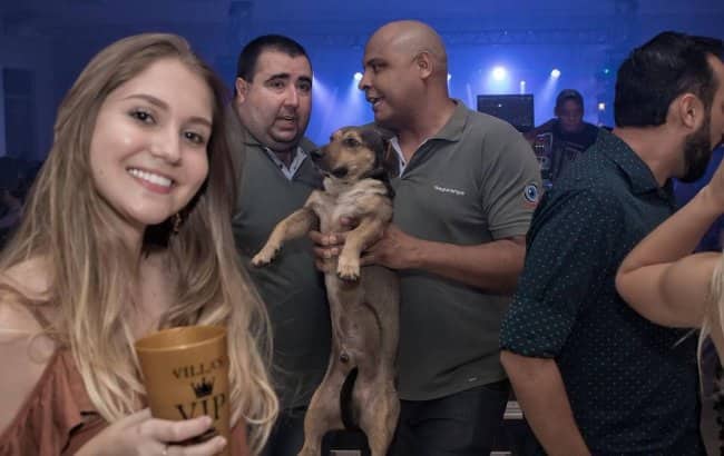 Nightclub security guard carrying a small brown dog out of a packed party venue.