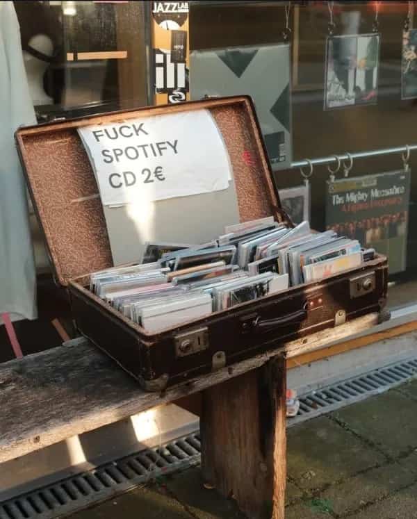 Funny meme showing a suitcase full of CDs with a handwritten sign reading fuck Spotify.