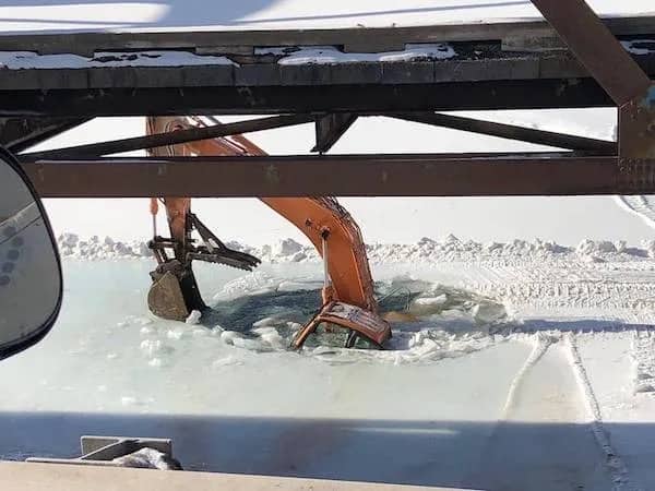 Orange construction excavator partially submerged in frozen water after breaking through a layer of ice.