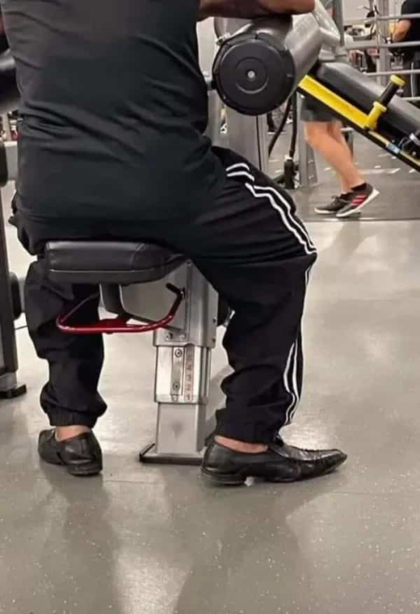 Funny gym meme showing a person working out on an exercise machine while wearing formal dress shoes.