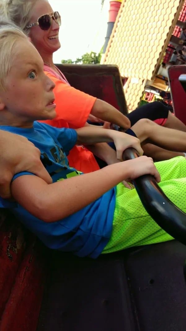 A blonde boy with wide, bulging blue eyes looking terrified while sitting on an amusement park ride.
