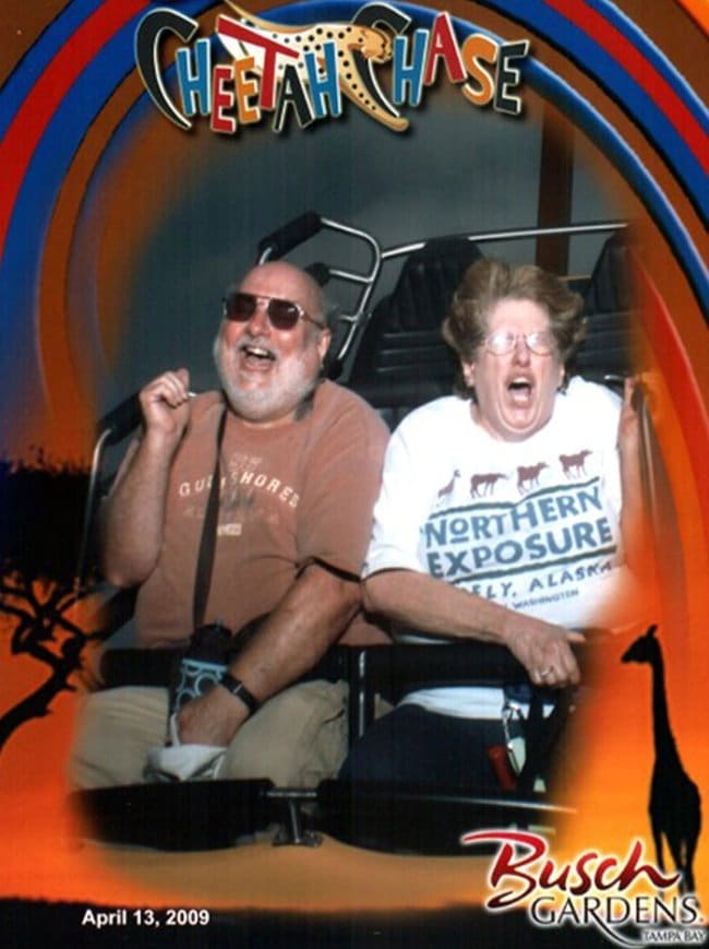 An older man laughing next to an older woman screaming in terror on a rollercoaster.