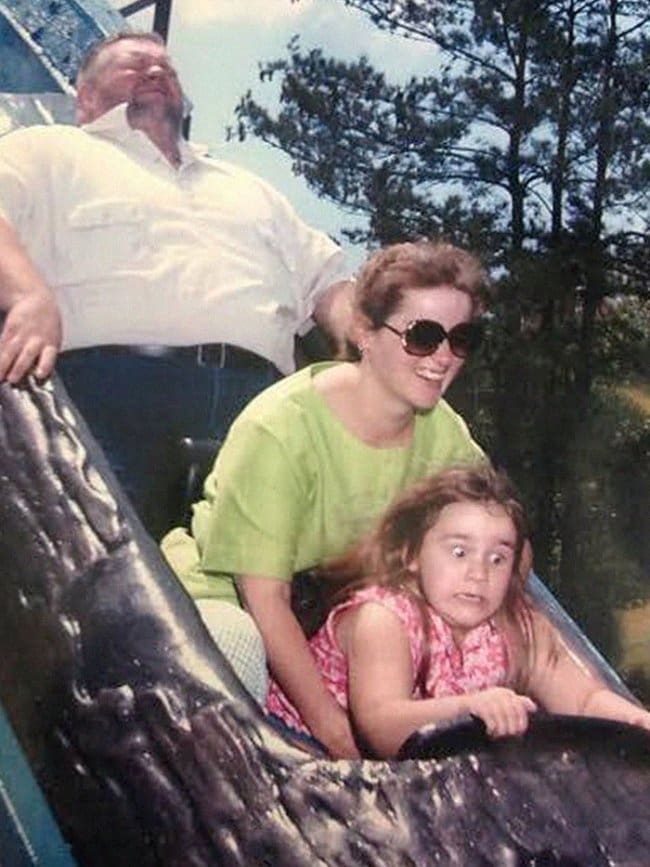 A young girl making a horrified face on a log flume drop while her mother smiles.