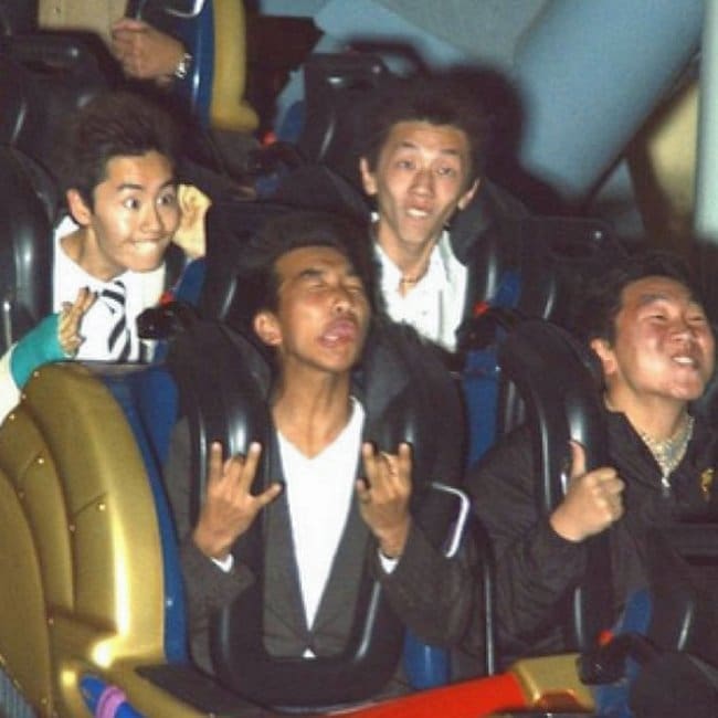 Four young men making hilarious, exaggerated panic faces as the rollercoaster camera flashes.