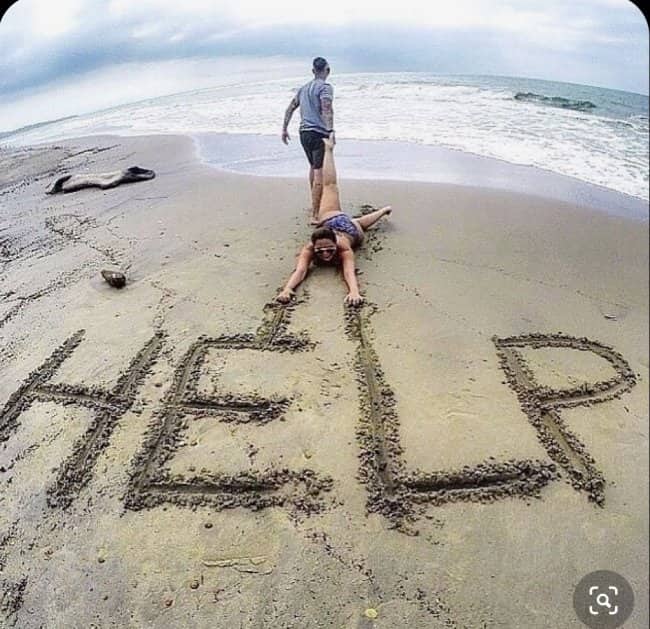 A woman dragged along the beach leaves trailing lines in the sand spelling out HELP.