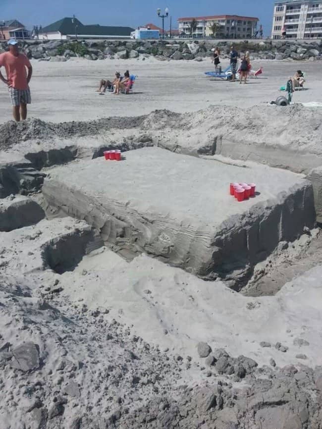 A giant beer pong table sculpted from sand with red plastic cups on top.