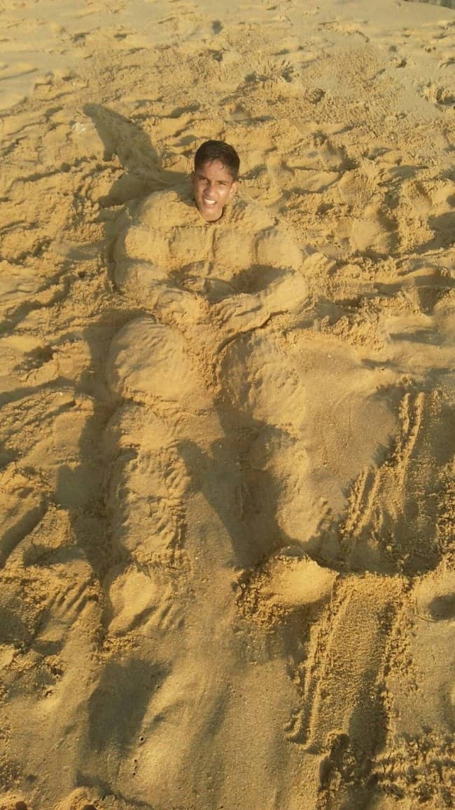 A man's head on top of a highly muscular body sculpted from sand.