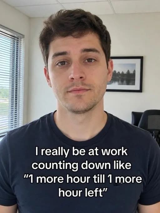 A highly relatable funny meme depicts a close-up portrait of a young man in a black t-shirt staring deadpan into the camera inside an office setting. The bold white overlay text reads: "I really be at work counting down like '1 more hour till 1 more hour left'", perfectly capturing the agonizing mental math of a slow shift.