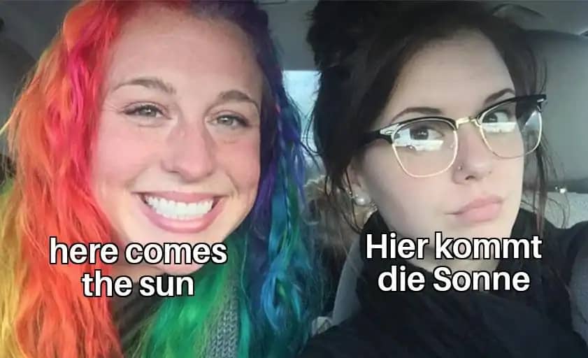 Two women in a car, one with colorful rainbow hair and another in dark clothing with glasses.