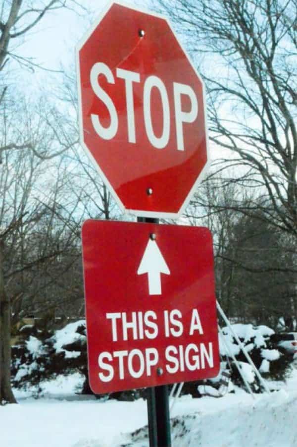 Red stop sign on a snowy street with an additional sign pointing to it.