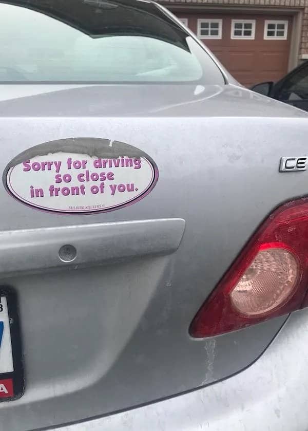 Silver car bumper with an oval sticker reading sorry for driving so close in front of you.