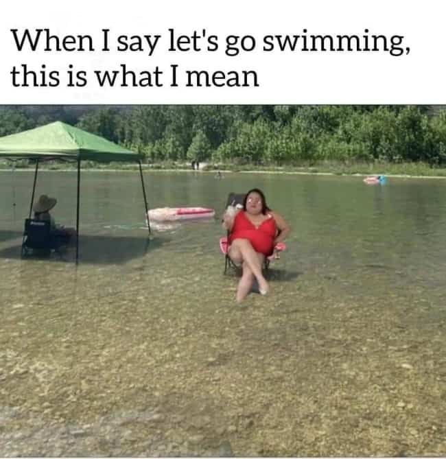Woman sitting lazily in a lawn chair submerged in shallow outdoor lake water drinking beverage.