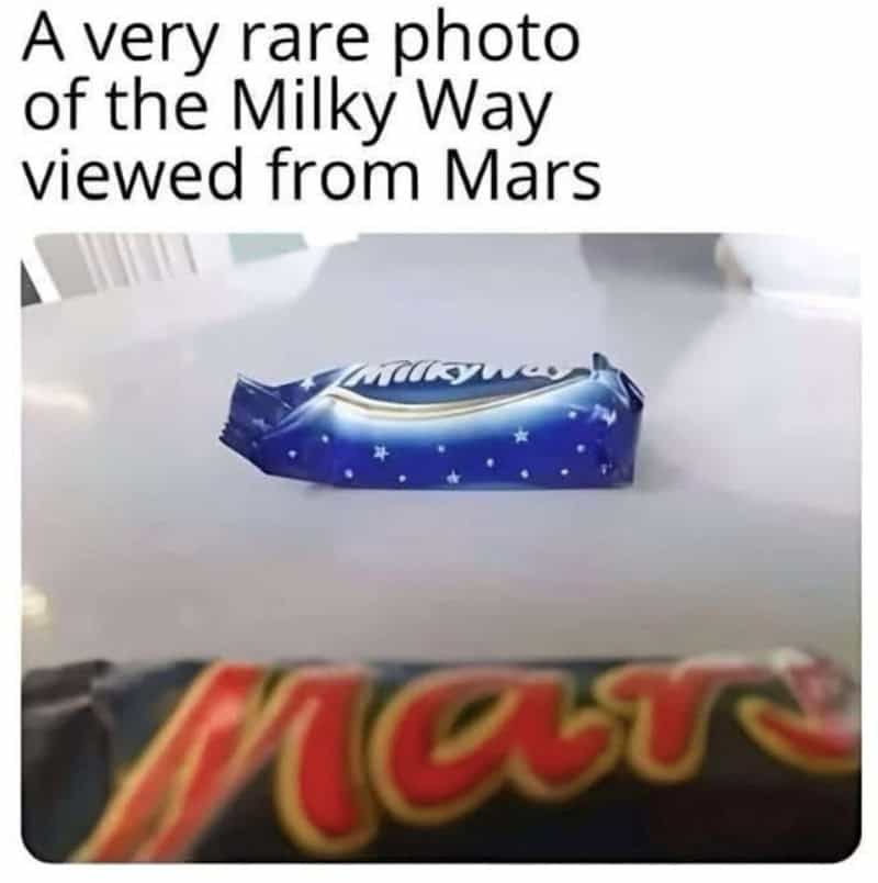 Milky Way candy bar placed on a table in front of a blurry Mars bar.