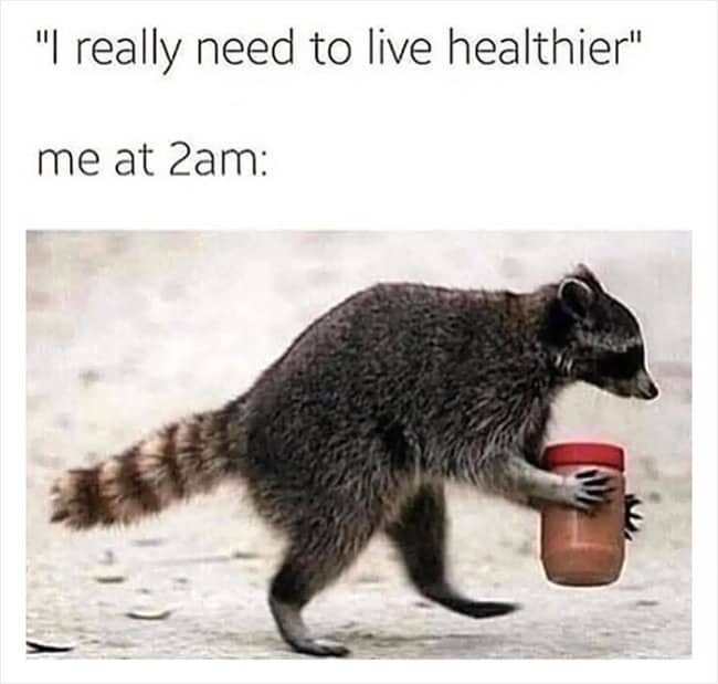 A raccoon walking down an outdoor path while carrying a full jar of peanut butter.
