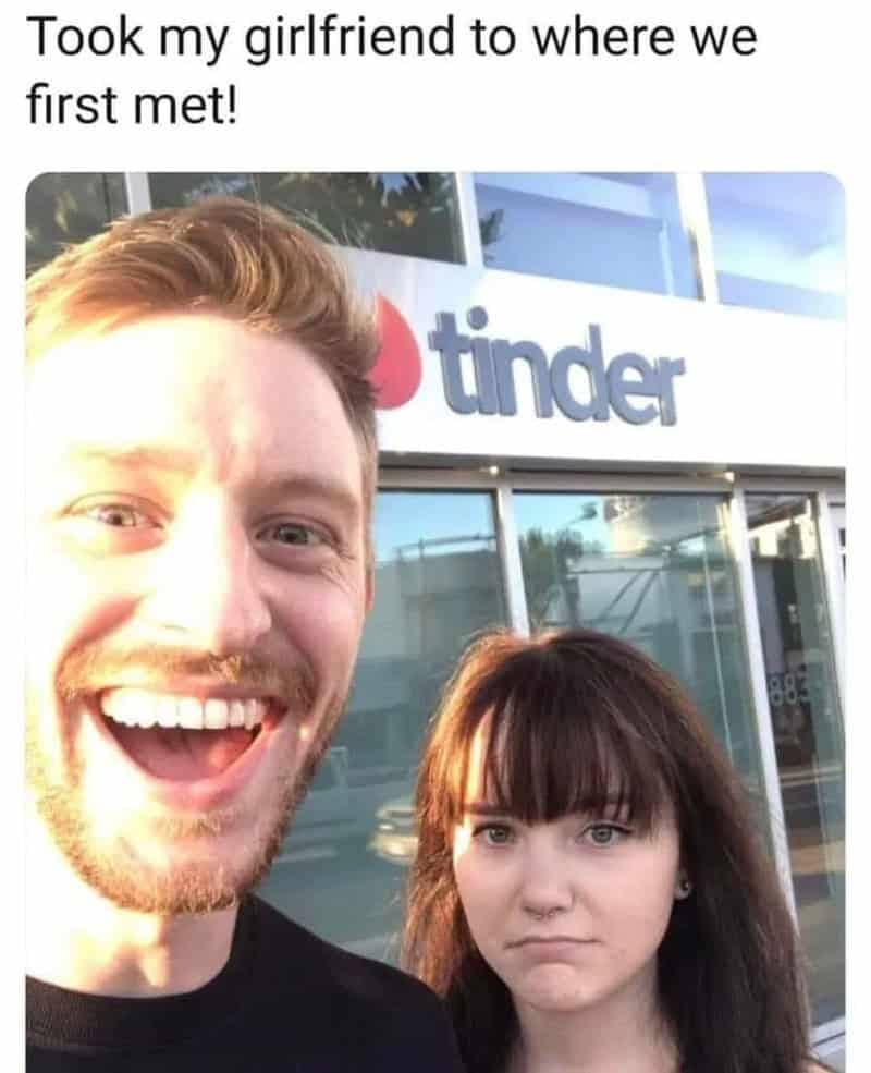 A smiling man and unamused woman posing outside of an official Tinder corporate building.