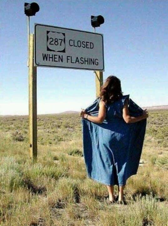 A cheeky road trip meme frames a woman taking a literal approach to a highway sign that reads "closed when flashing" by opening her denim dress up to it.