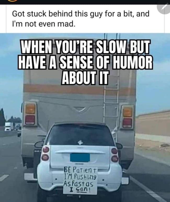 That viral road trip meme features a tiny white compact car being towed behind a massive motorhome with a handwritten sign claiming it's pushing as fast as it can.