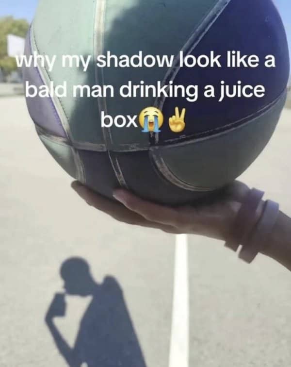 A basketball shadow on the concrete pavement that looks exactly like a bald man drinking a juice box.