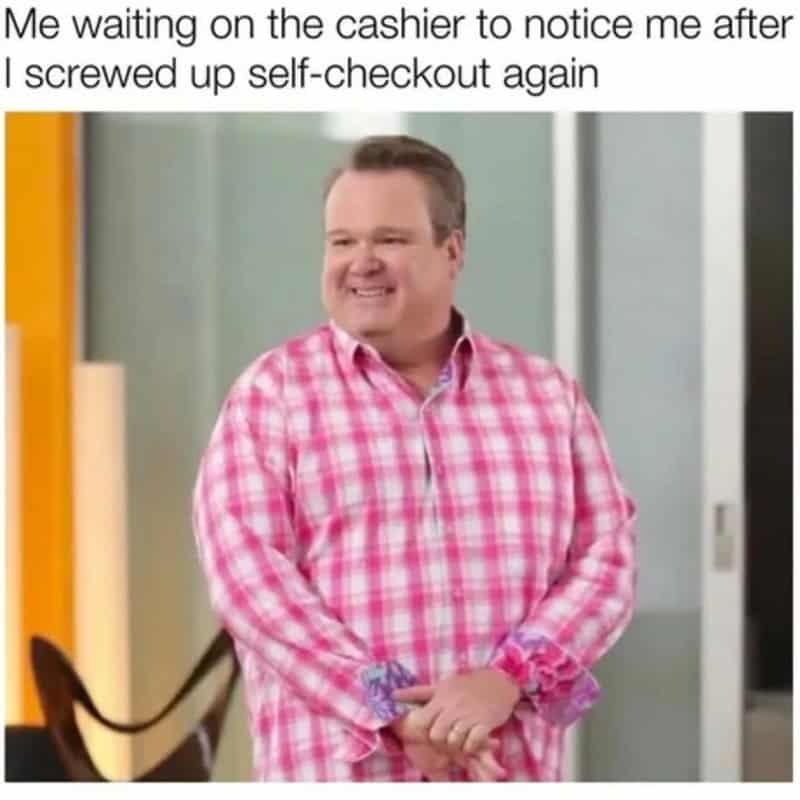 Modern Family character smiling nervously waiting for self-checkout clerk to clear register error.