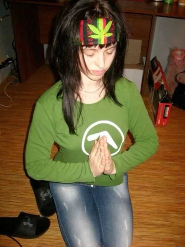 A girl wearing a marijuana leaf headband praying on a wooden floor.