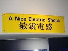 A yellow warning sign featuring a funny translation mistake reading "A Nice Electric Shock."