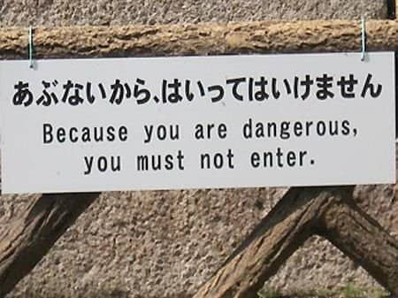 A wooden fence sign featuring a translation fail that calls the reader dangerous.