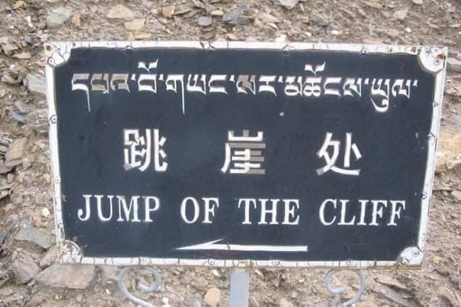 A black trail warning sign showing a bad translation that reads "JUMP OF THE CLIFF."