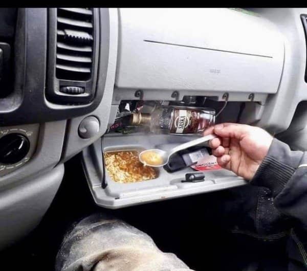 Person eating hot ramen soup directly out of their car's open glove compartment console.