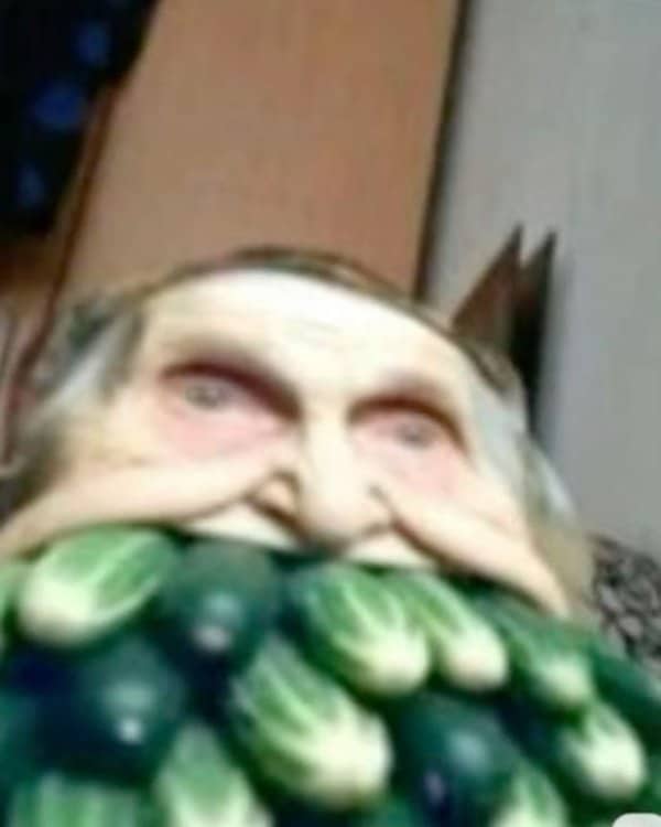 Blurry close-up photo of a face stuffed with dozens of small green cucumbers.